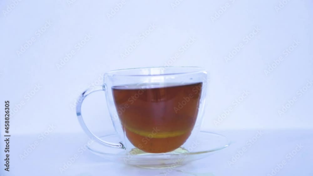 A mug of black tea stands on a white background, a ring of yellow lemon is thrown into it, splashes. A mug of black tea stands on a white background, a ring of yellow lemon is thrown into it, splashes.