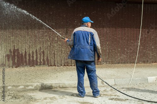 A man washes the fence with a hose. The builder cleans the fence from dirt.