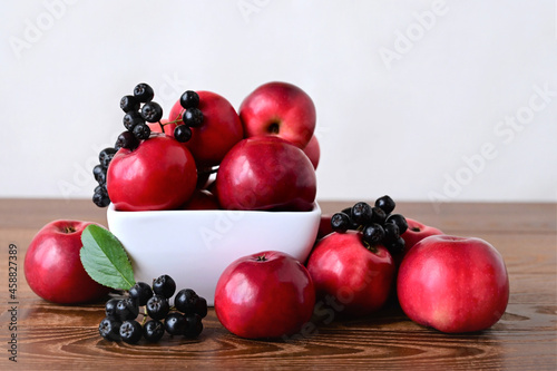 beautiful autumn still life of red apples and chokeberry lying on wooden table on white background. Colorful nature. Harvest time. Copy space