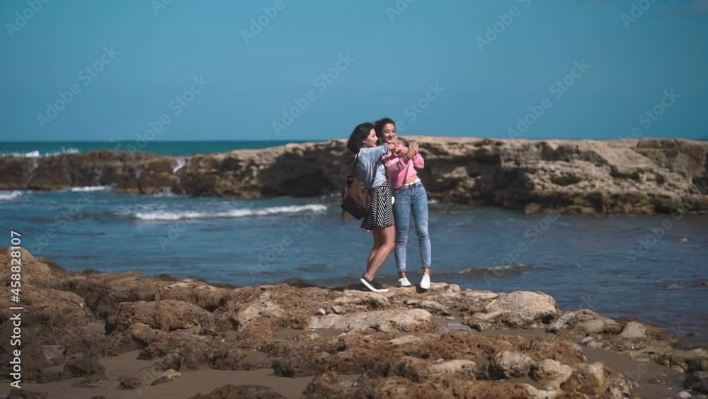 Happy girls making selfie on a rock over the sea. Best friends spend summer time together. The girls are happy and enjoy life. The road by car to the sea. Friendship and love forever. The beauty of Happy girls making selfie on a rock over the sea. Best friends spend summer time together. The girls are happy and enjoy life. The road by car to the sea. Friendship and love forever. The beauty of