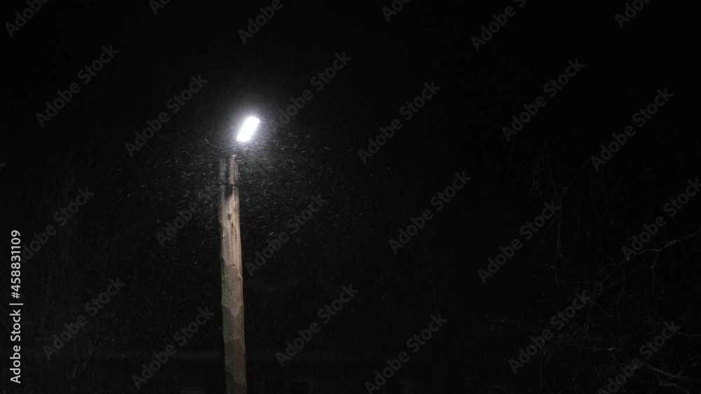 street lamp and night snowfall, snow flakes in the light of the lamp, dark night