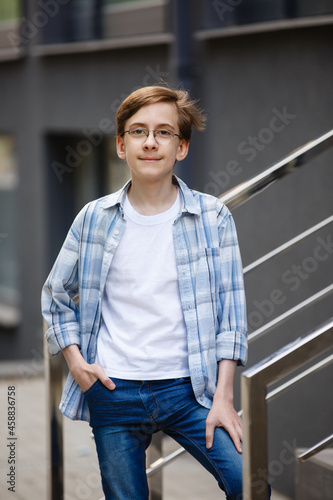 Teenager boy in casual blue denim outfit on background of the City. Fashion style guy classic portrait. Street style male portrait looking to camera. Modern urban boy's walk in a town