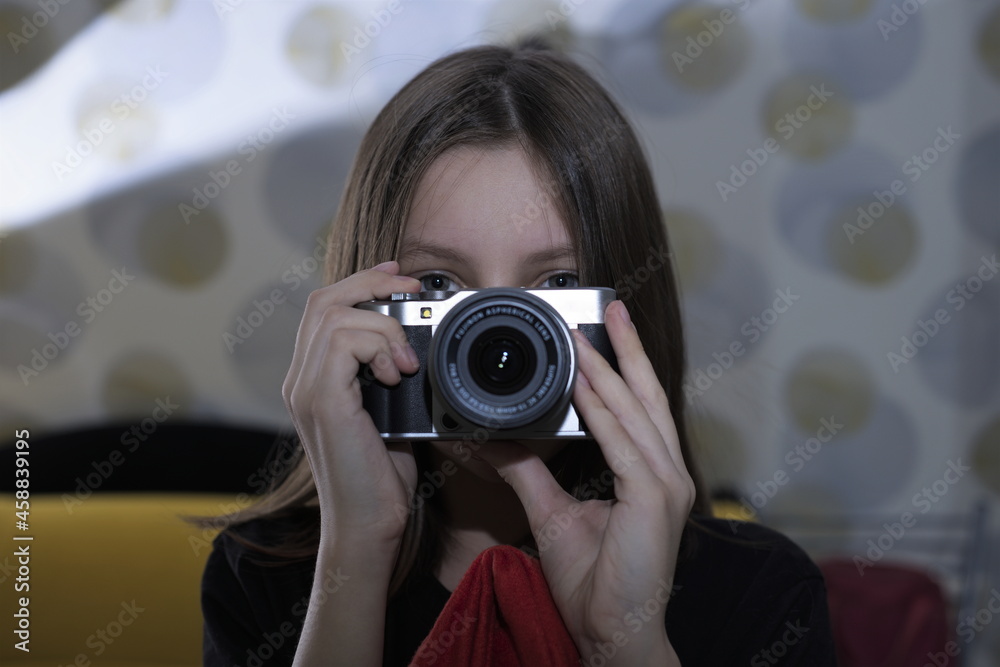 Portrait of a teenage girl with a camera in her hands, looking straight. A woman with an old camera takes pictures. Blurred background. Teenage blogger photo. Portrait of a teenage girl with a camera in her hands, looking straight. A woman with an old camera takes pictures. Blurred background. Teenage blogger photo.