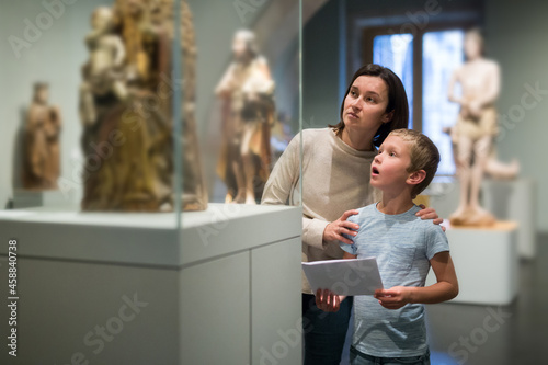 Attentive young woman with school age boy visiting sculptures exposition in museum