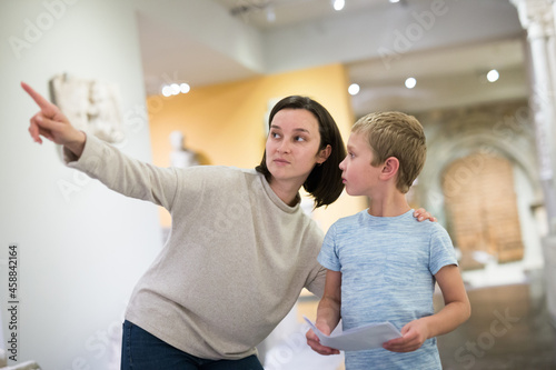 Fototapeta Naklejka Na Ścianę i Meble -  Attentive young woman with school age boy visiting sculptures exposition in museum, pointing to something