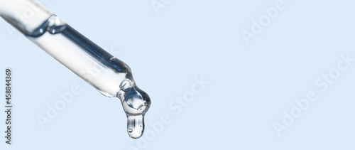 Cosmetics dropper, falling drop close up. Closeup of cosmetic pipette with essential oil dropping, serum with peptides on blue background. Self care concept. Beauty skin care product. Banner