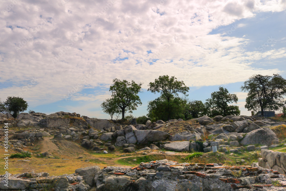 landscape with an uneven rocky surface with trees, stones, dry grass and a blue sky with clouds in the background - Roman ruins on Nevet Tepe hill in Plovdiv, Bulgaria