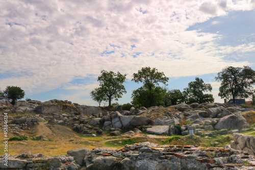 landscape with an uneven rocky surface with trees, stones, dry grass and a blue sky with clouds in the background - Roman ruins on Nevet Tepe hill in Plovdiv, Bulgaria