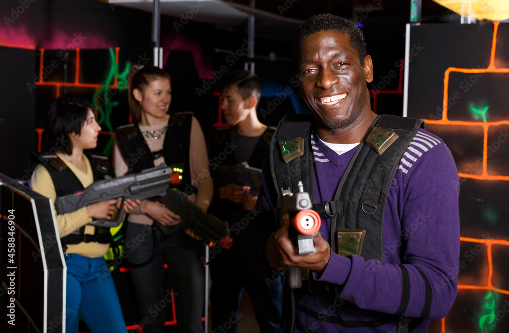 Portrait of confident African laser tag player with gun ready for game in dark labyrinth..