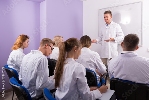 Adult male student answering near whiteboard in front of teacher and group of students in auditorium