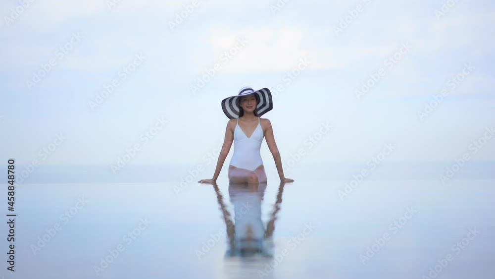 A pretty woman in a white one-piece bathing suit and huge, floppy straw ...