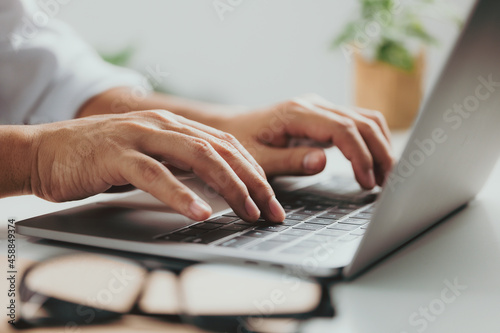 Close-up of man hands typing on laptop keyboard on white table at home office or workplace.