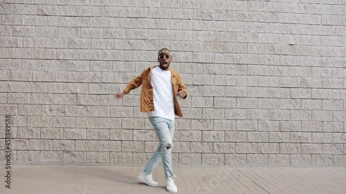 Dance loop of joyful African American student jumping dancing looking at camera outdoors against urban wall background. People and creativity concept.