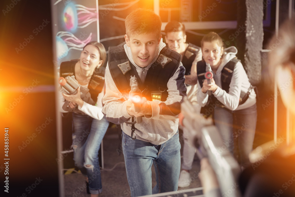 Obraz premium Portrait of happy young man with laser pistol and playing laser tag with his friends in dark room. High quality photo