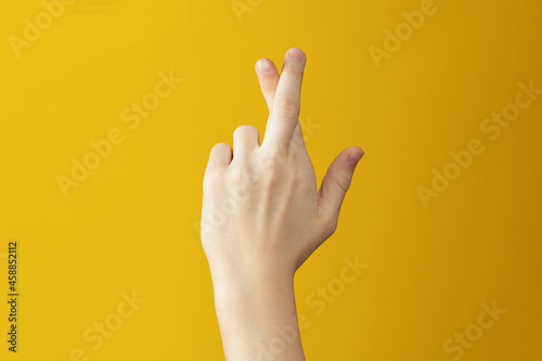 Hand on orange background showing fingers which are crossed. Gesture wishing good luck