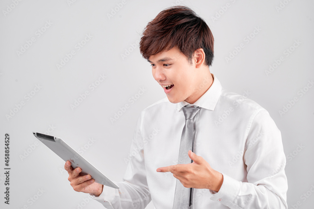 Handsome young asian man holding digital tablet and looking at it with smile while standing against white background Handsome young asian man holding digital tablet and looking at it with smile while standing against white background