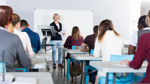 Female speaker giving presentation for adult students in lecture hall .