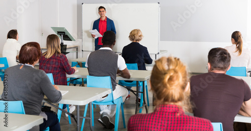 Friendly male teacher lecturing to attentive adult students at auditorium