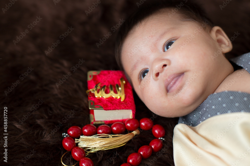 A cute Asian infant Muslim in thobe and rosary beads on red, muslim