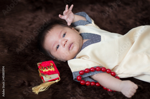 A cute Asian infant Muslim in thobe and rosary beads on red, muslim bead on bed in the home, translation is the name of muslim God 