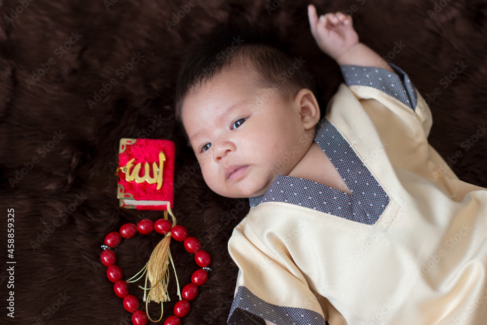A cute Asian infant Muslim in thobe and rosary beads on red, muslim
