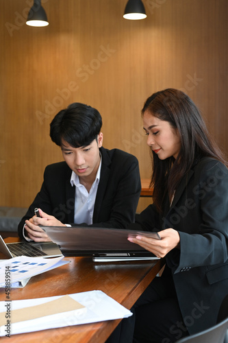 Two business partners discussing financial reports together in modern workplace.