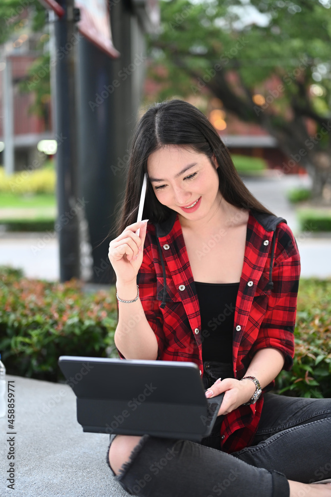 Cheerful young woman sitting in the city park and using digital tablet. Cheerful young woman sitting in the city park and using digital tablet.