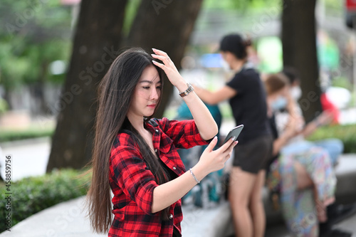 Beautiful Asian woman using smart phone while sitting in the city park.