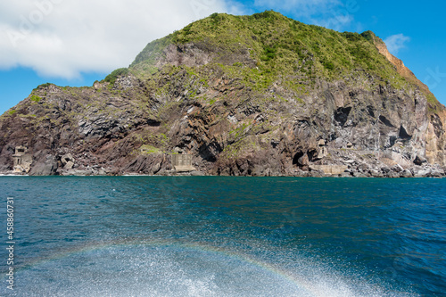The waves of the yacht next to the island reflect a short rainbow
