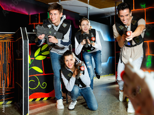 Modern positive smiling young people with laser pistols playing laser tag on dark labyrinth