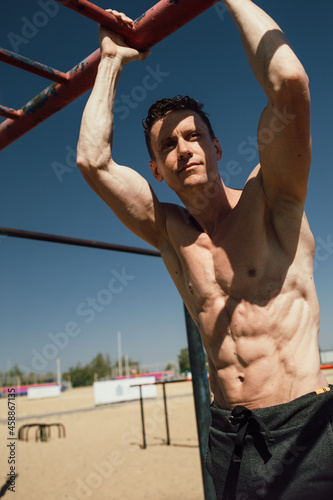 Young Man Doing Calisthenics Outdoors. Man Doing Pull-Ups in the Street. Guy Working Out on Pull-Up Bars. Man Exercising Outdoors. Sport Concept.