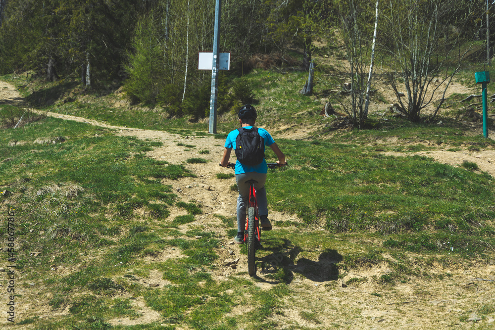 Młody rowerzysta na ebike jedzie lasem pod górę. - obrazy, fototapety, plakaty 