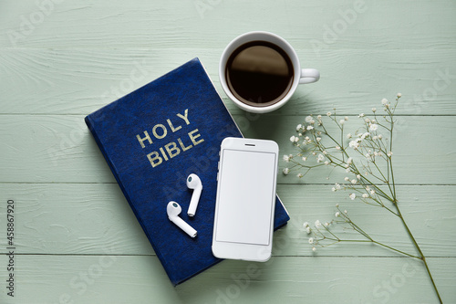 Holy Bible, earphones, mobile phone, gypsophila flowers and cup of coffee on color wooden background