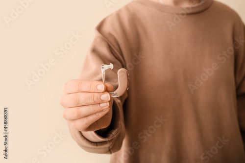Woman with hearing aid on color background, closeup