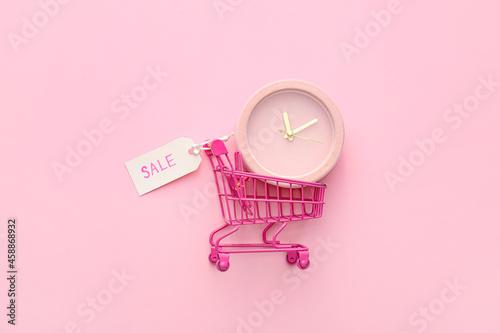 Alarm clock in small shopping cart on pink background, top view photo