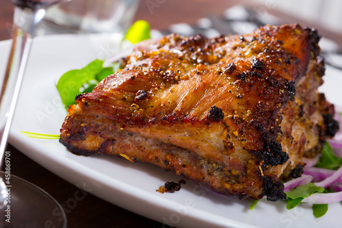 Appetizing broiled rack of pork with vegetable garnish of fresh red onion and greens..