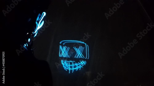 Neon mask with glow, boy with hood, reflection on the glass, mirror effect. Halloween and horror concept. photo