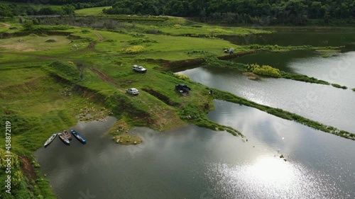 Aerial footage over the water towards the edge of the forest revealing boats, vehicles people, fishing and enjoying nature, Muak Klek, Saraburi, Thailand. photo