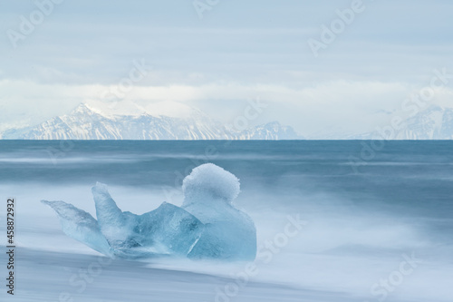 Iceberg shaped like a swan on the beach at Jokulsarlon with mountains and sky in the background. 