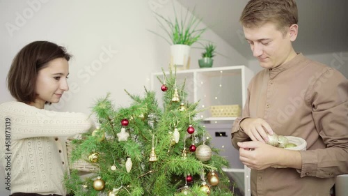 Happy family decorates the Christmas tree with red and gold balls in their home. A couple, a young woman and a man are preparing for the new year and Christmas holidays.