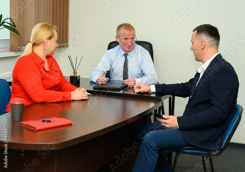 Focus on the man in the center. A team of three adult managers sitting at a desk in an office condemning cases photo