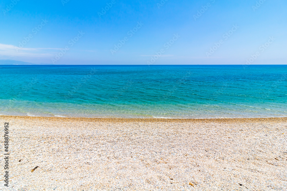 Pebbles on the beach and turquoise sea against clear blue sky. Summer background