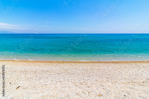 Pebbles on the beach and turquoise sea against clear blue sky. Summer background