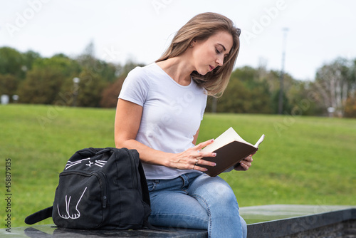 A young, happy and attractive Caucasian girl is sitting in the park and reading a book. Education concept. © Павел Костенко