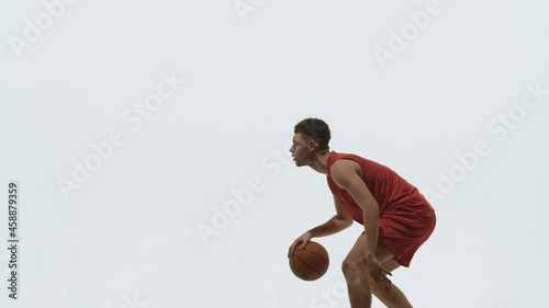 Guy basketball player dribbling ball, hitting it on floor and throws into basket. Young athlete trains before streetball competition. Picture taken in the studio on a white background in slow motion. photo