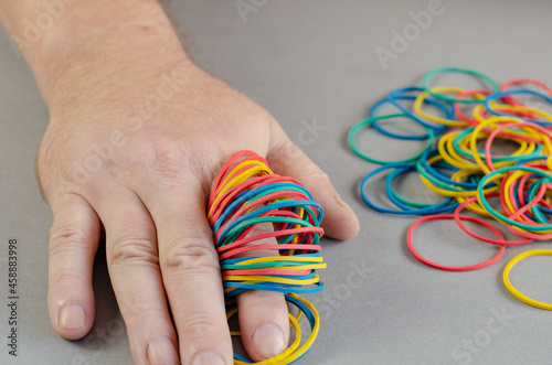 One man's arm and stationery rubber bands on a gray background. Multicolored round rubber bands strung on the index finger. Stationery. Close-up. Selective focus.