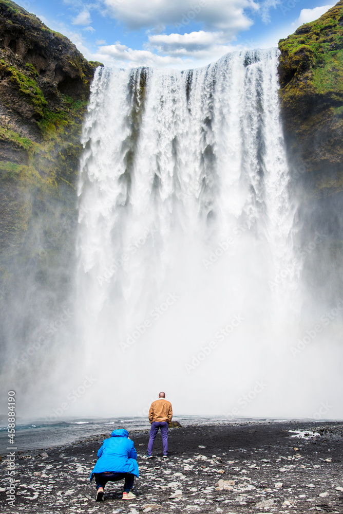 Man photographing his friend on background Skogafoss waterfall in Iceland. Exotic countries. Amazing places.