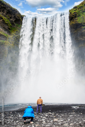 Man photographing his friend on background Skogafoss waterfall in Iceland. Exotic countries. Amazing places.