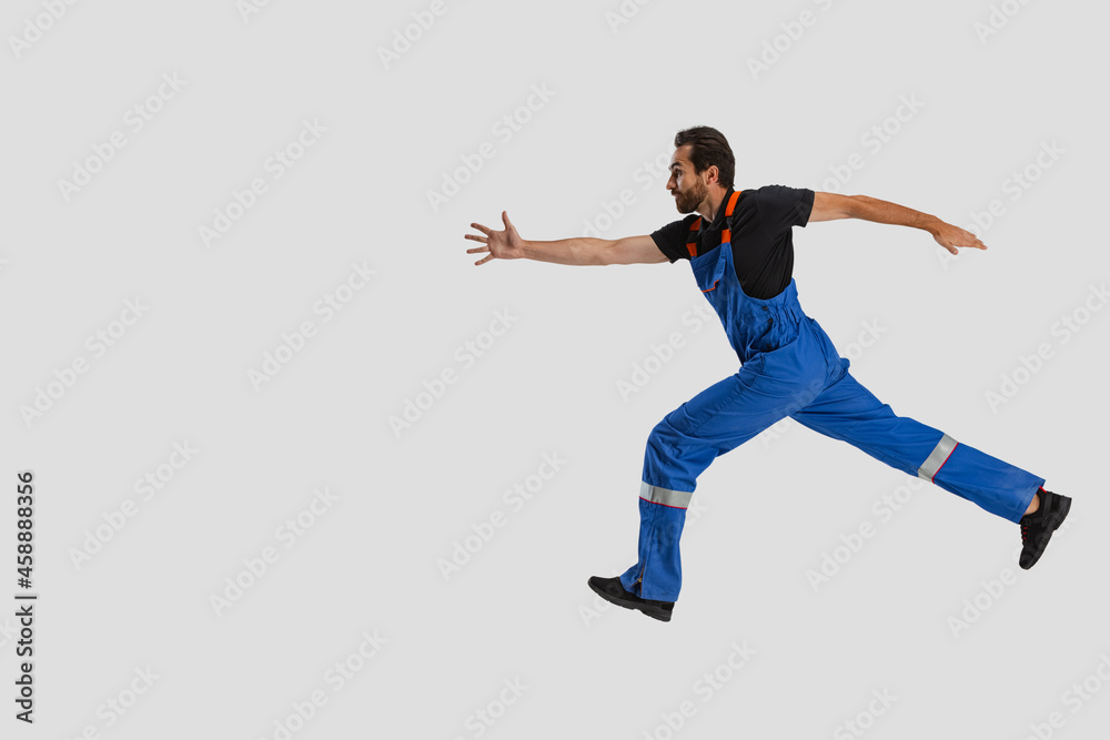 Portrait of young man, male auto mechanic in dungarees running isolated over white studio background. Concept of labor, occupation, funny meme emotions