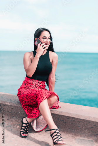 Young woman is sitting on the street during talking by phone and looking forward. Connecting people concept